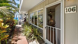 A covered walkway with a view of the ocean, a door labeled '106', and various tropical plants.