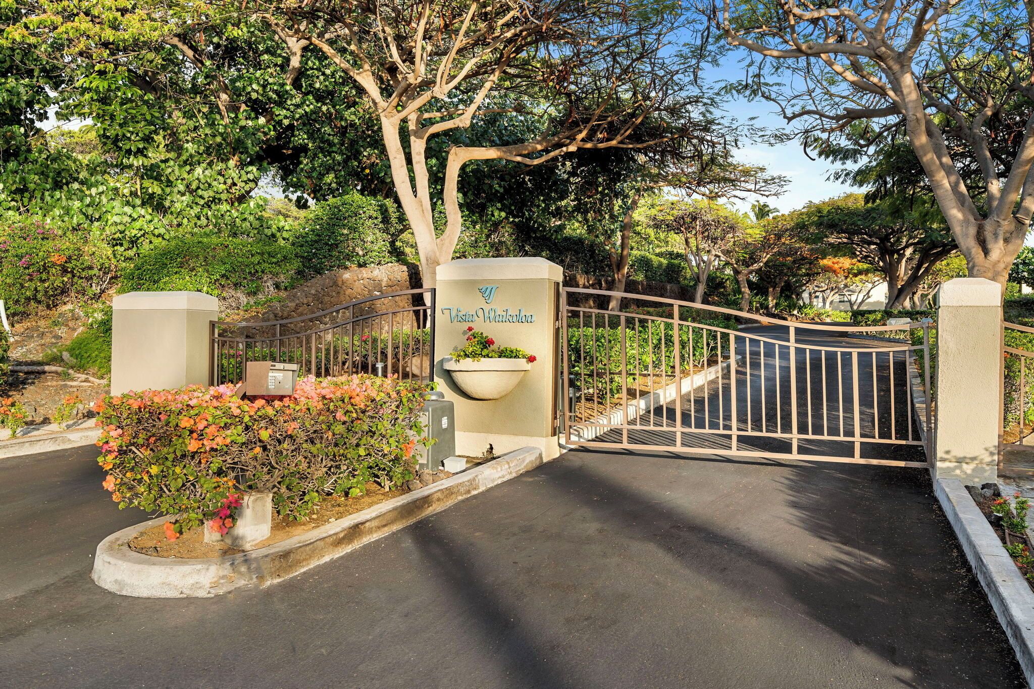 A gated entrance with a sign reading "Vista Waikoloa" and a flower bed with pink flowers.
