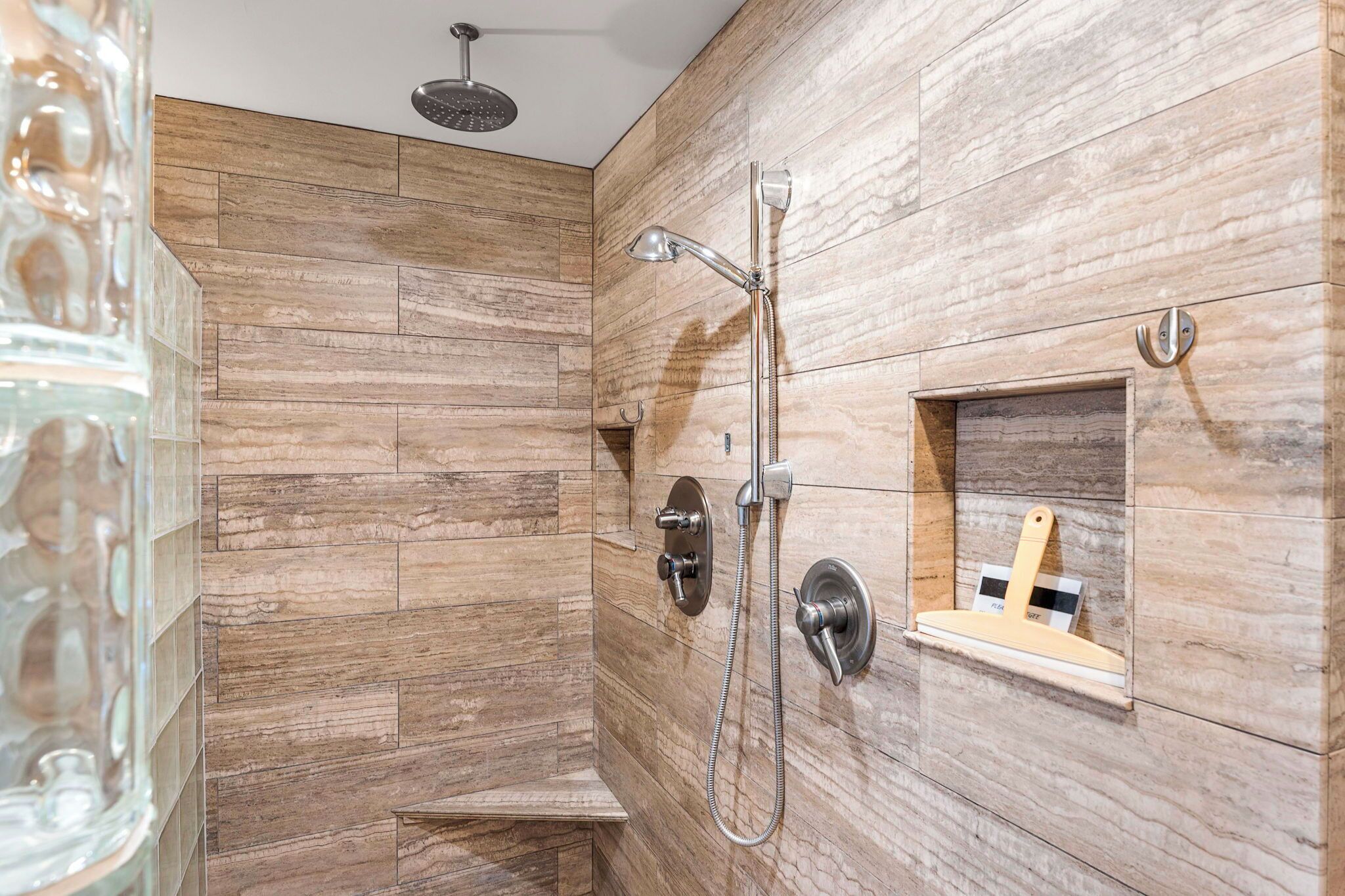 A modern shower with a handheld showerhead and a wall-mounted faucet, set against a wooden wall.