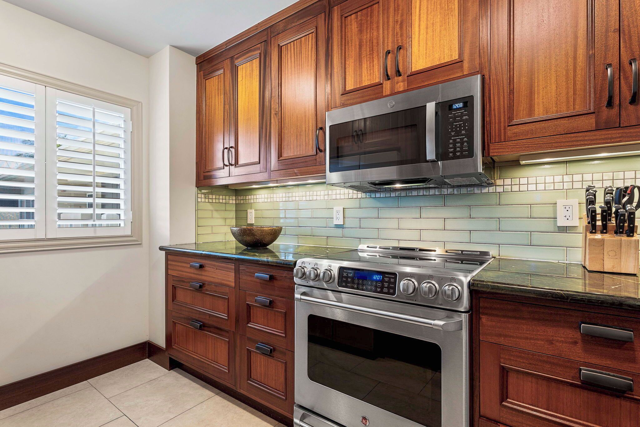 A kitchen with wooden cabinets, a stainless steel stove, a microwave, and a tiled backsplash.