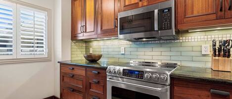 A kitchen with wooden cabinets, a stainless steel stove, a microwave, and a tiled backsplash.