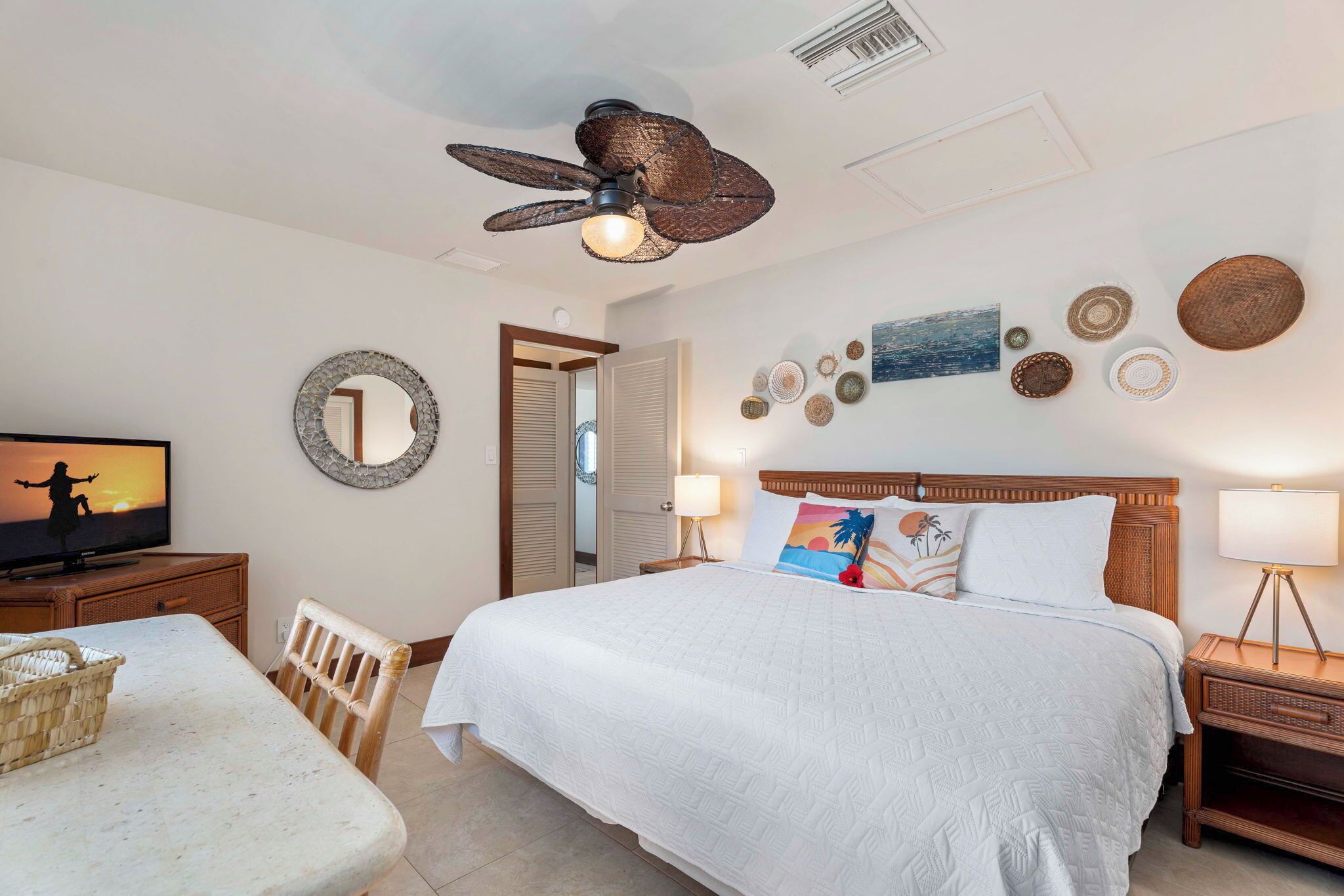 Een slaapkamer met een groot bed, een plafondventilator, een televisie en een muur versierd met diverse objecten.