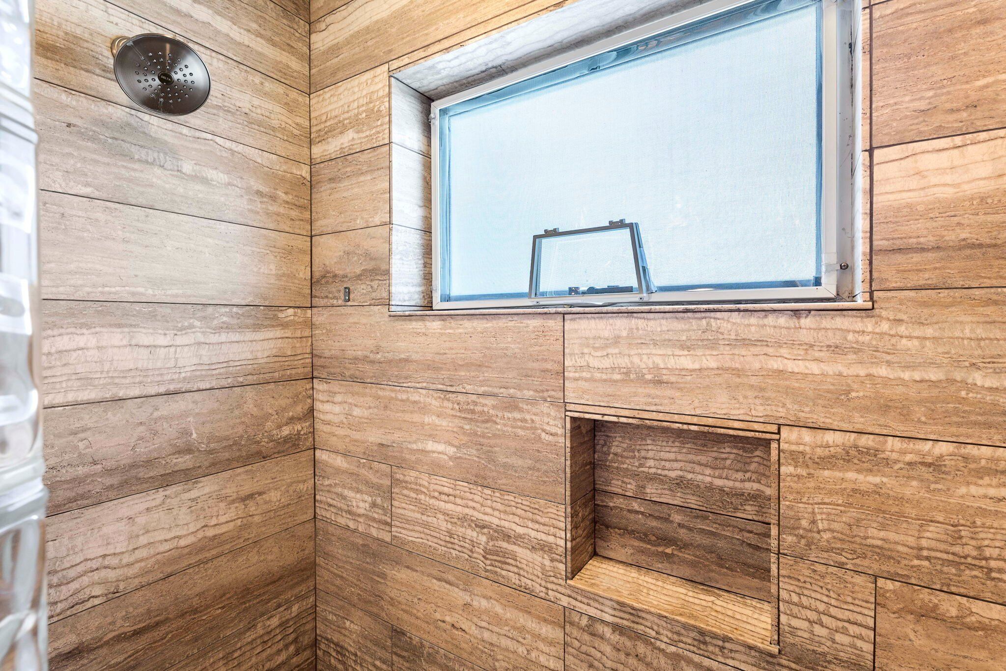 A bathroom with wooden paneling, a window, and a showerhead.