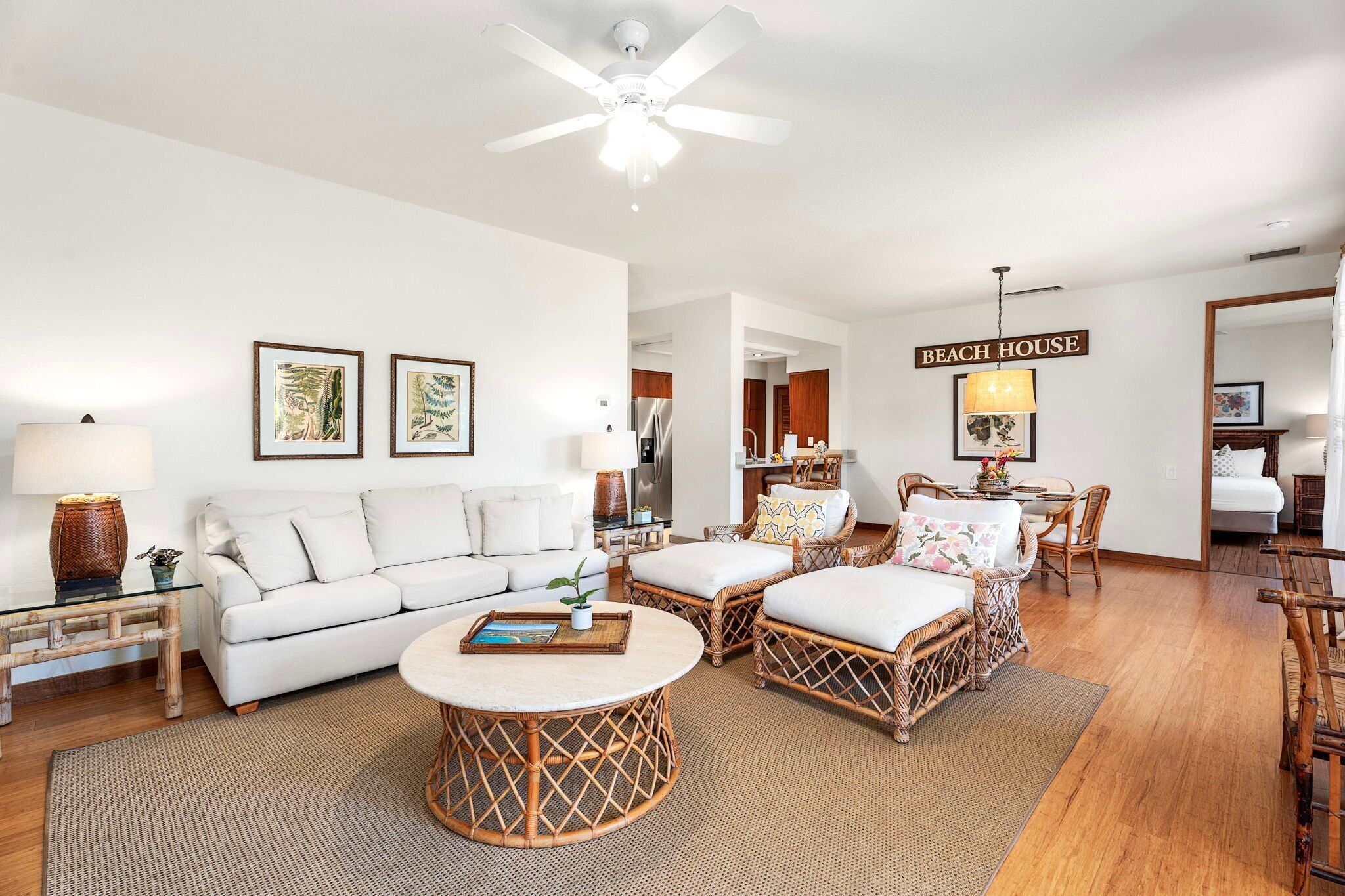 A spacious living room with a white sofa, wicker chairs, a round coffee table, and a ceiling fan.