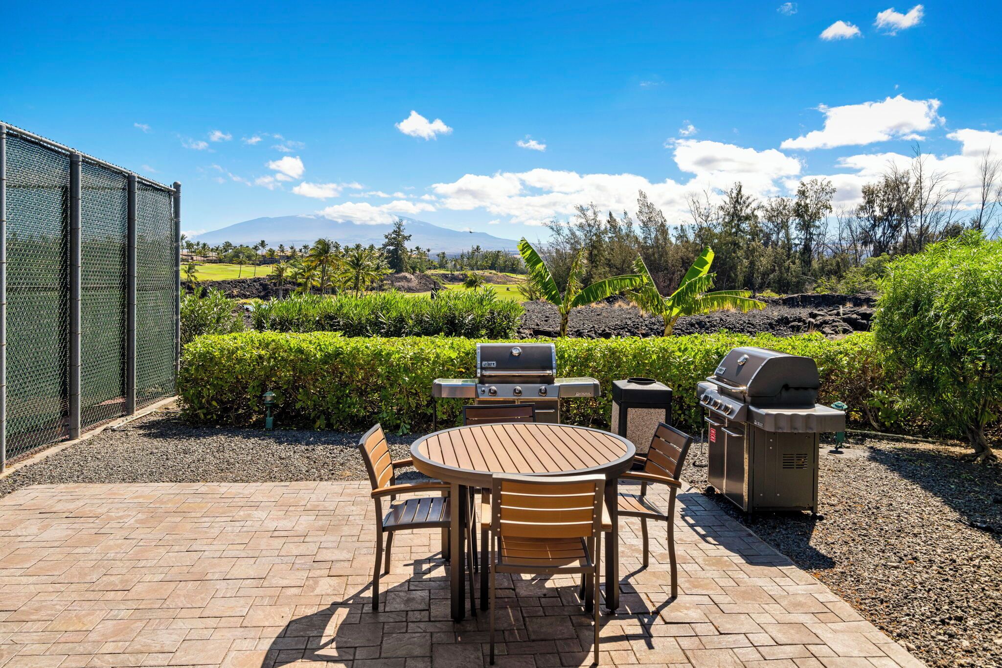 An outdoor patio with a round wooden table and chairs, a grill, and a barbecue.