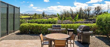 An outdoor patio with a round wooden table and chairs, a grill, and a barbecue.