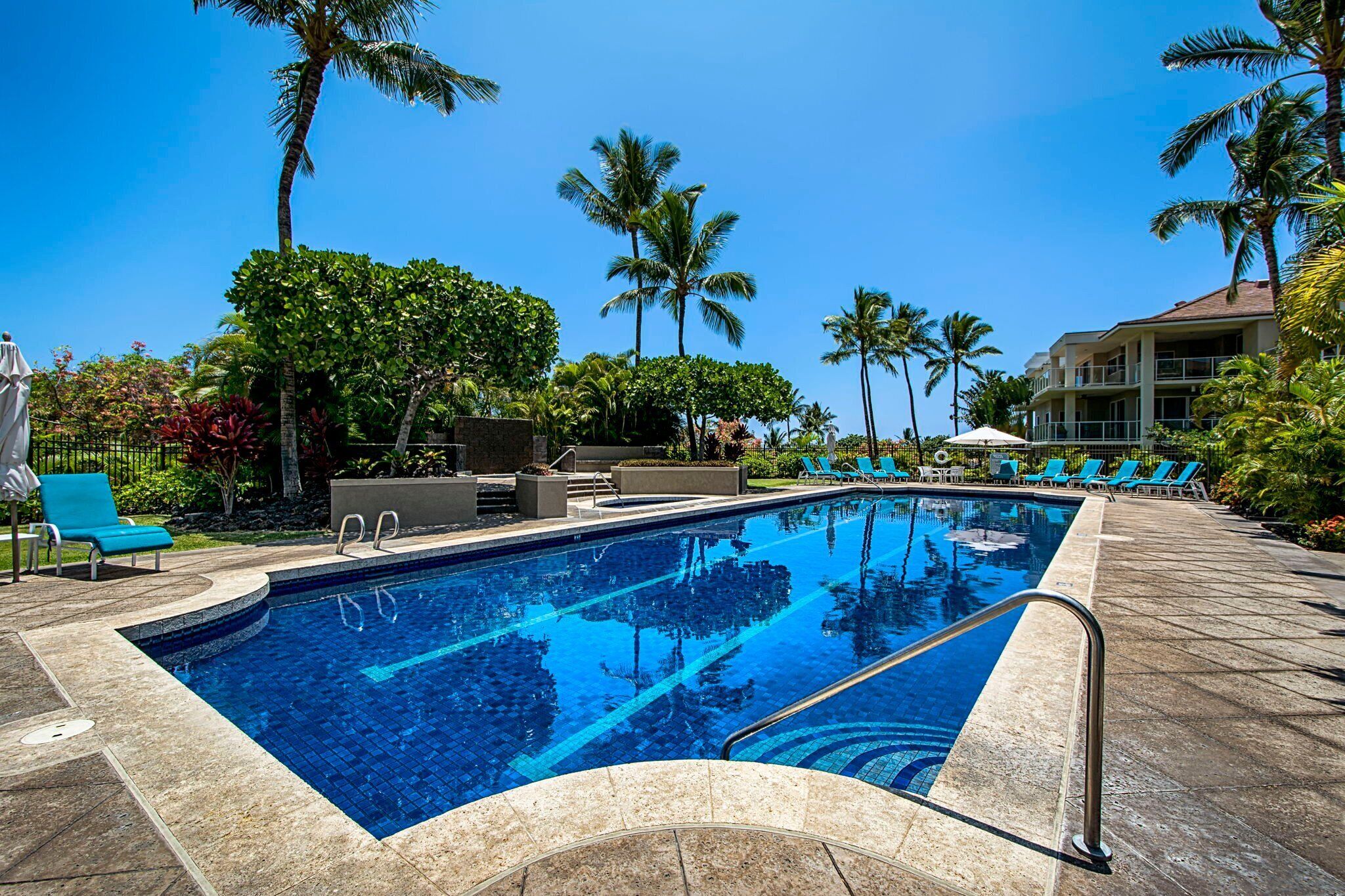 Una piscina con sillones de descanso y palmeras.