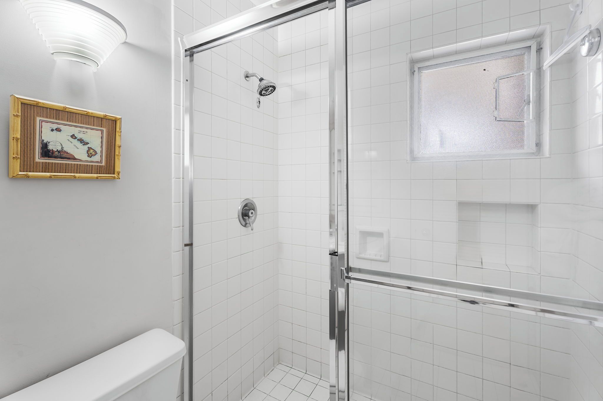 A modern bathroom with a glass-enclosed shower, white tiled walls, and a framed picture on the wall.