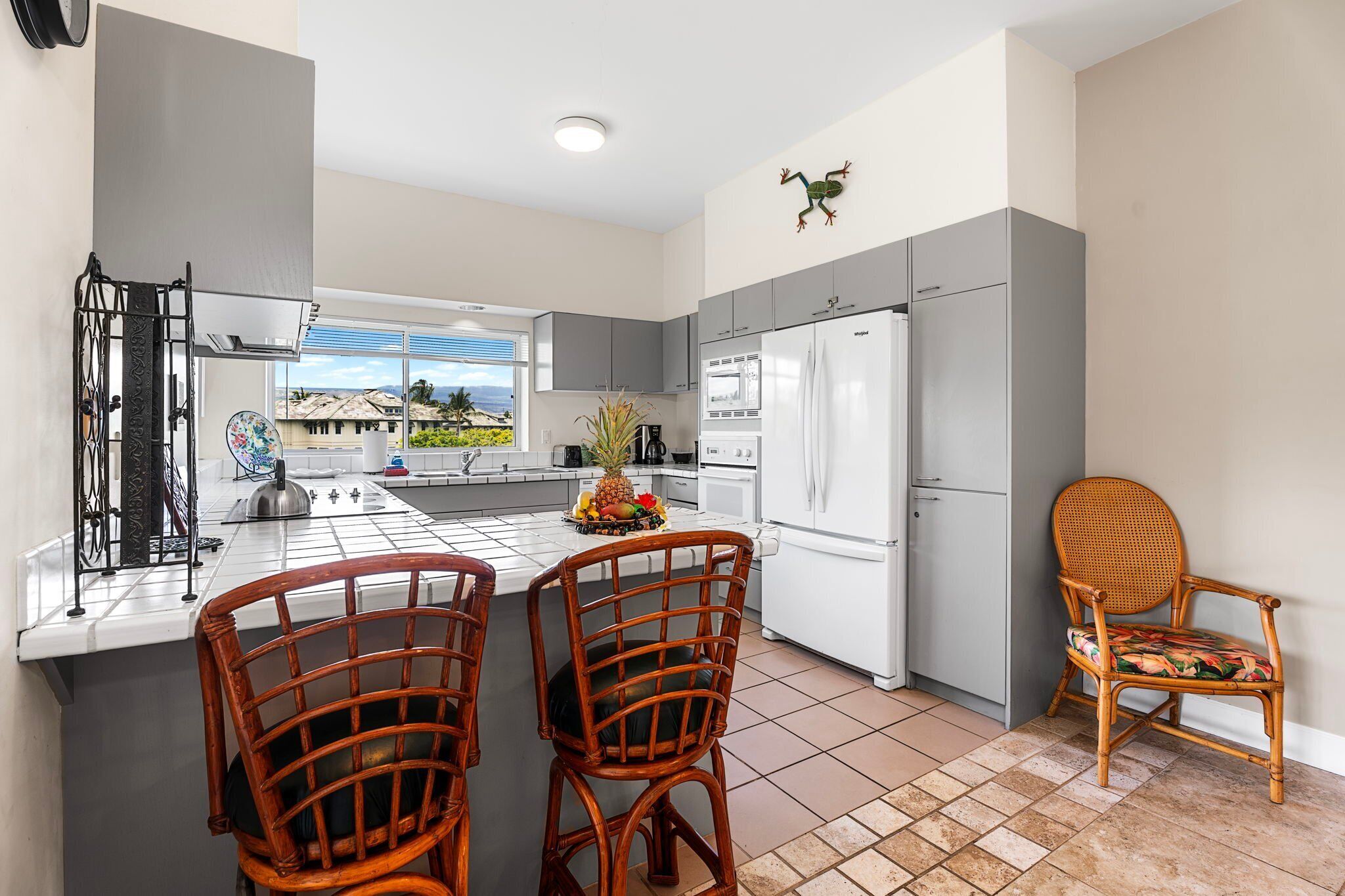 A modern kitchen with grey cabinets, a white refrigerator, and a dining area with wicker chairs.