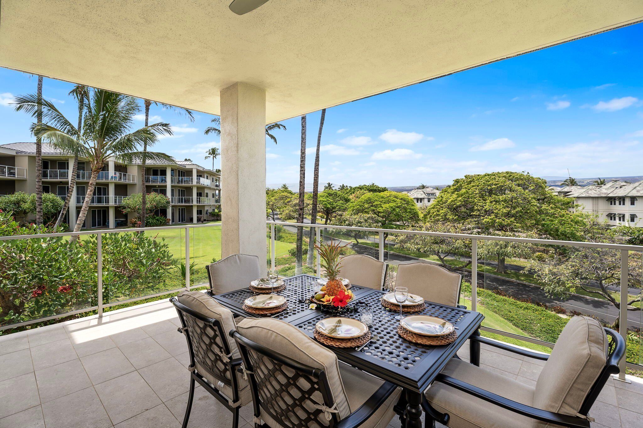 A balcony with a table set for dining, overlooking a residential area with palm trees and a clear sky.