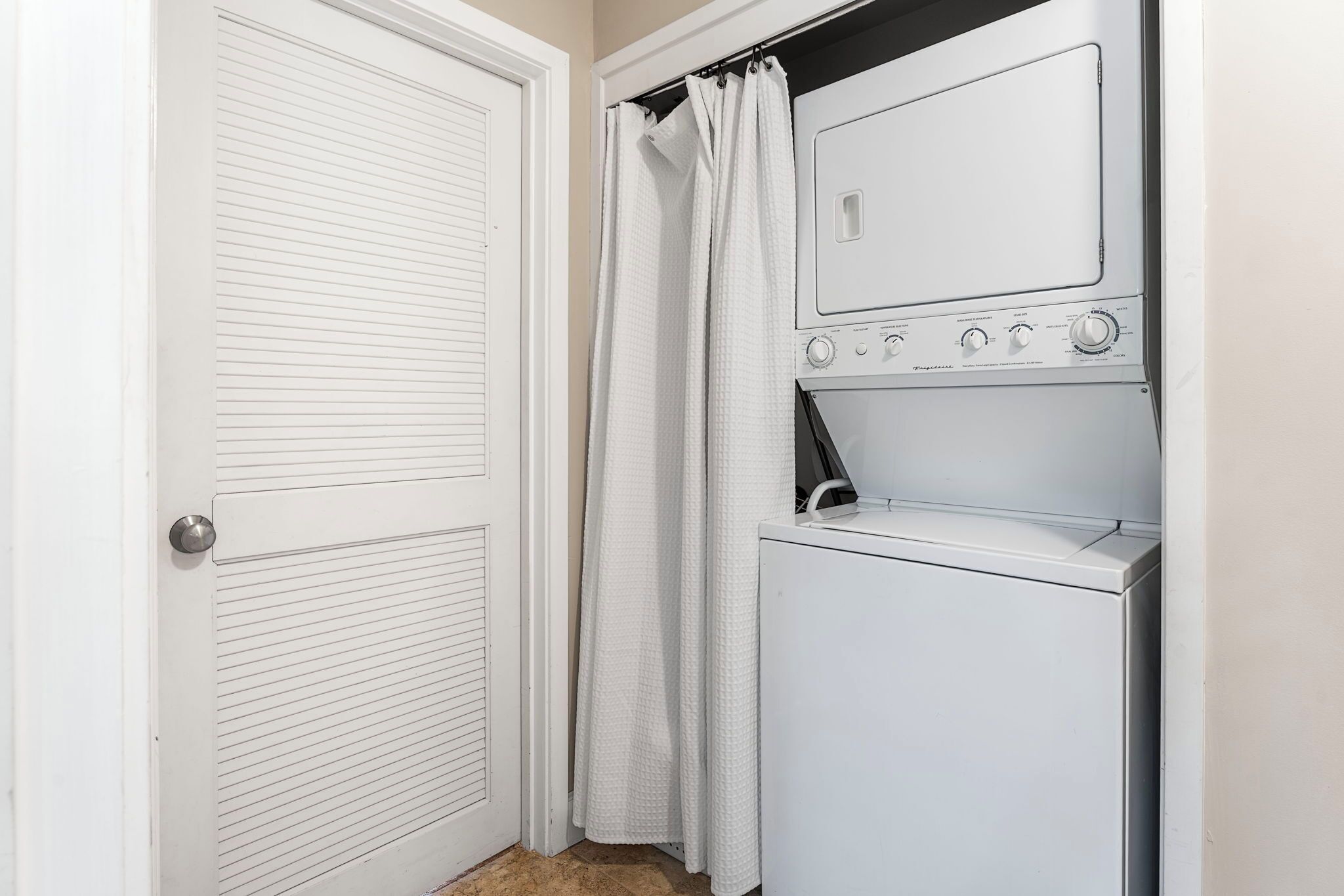 A laundry room with a white dryer and washing machine, a white door, and a shower curtain.