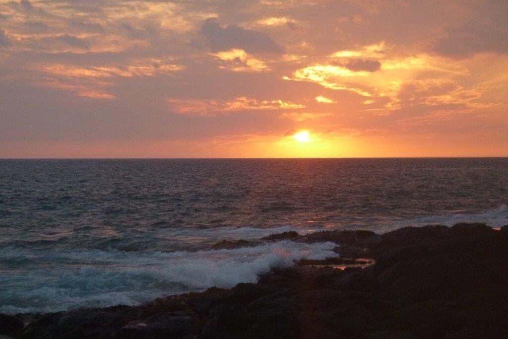 A sunset over the ocean with waves crashing against rocks.