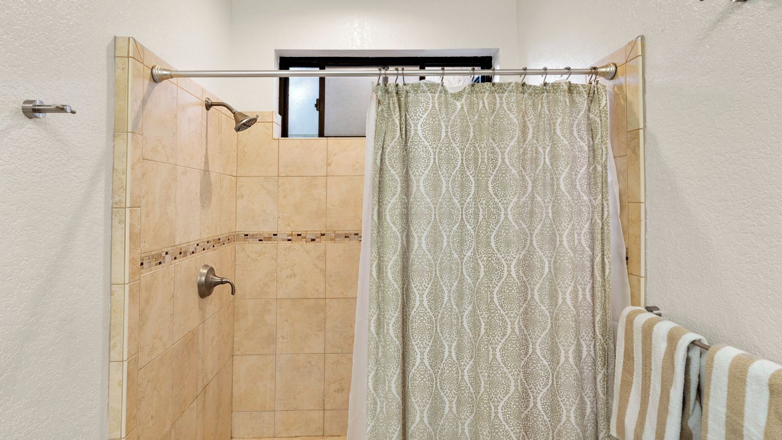 Une douche aux carreaux de couleur beige, un pommeau de douche et un rideau orné d’un motif cachemire.