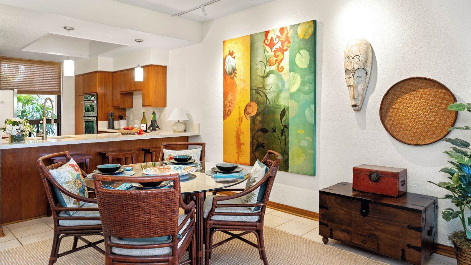 A dining area with a round table, wicker chairs, and a colorful abstract painting on the wall.