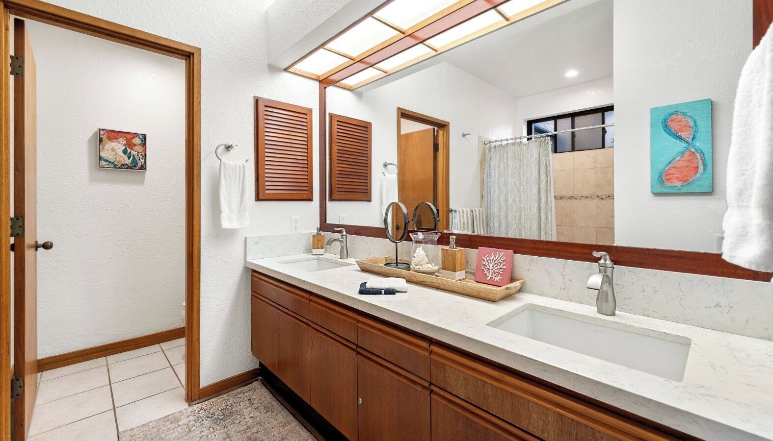 A modern bathroom with a double sink vanity, wooden cabinets, and a large mirror.