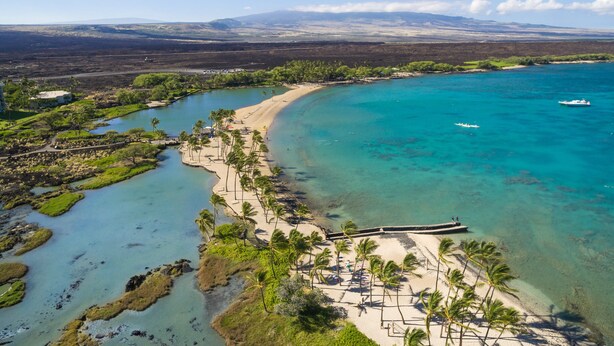 Un resort costero con una playa arenosa, palmeras y aguas turquesas cristalinas.