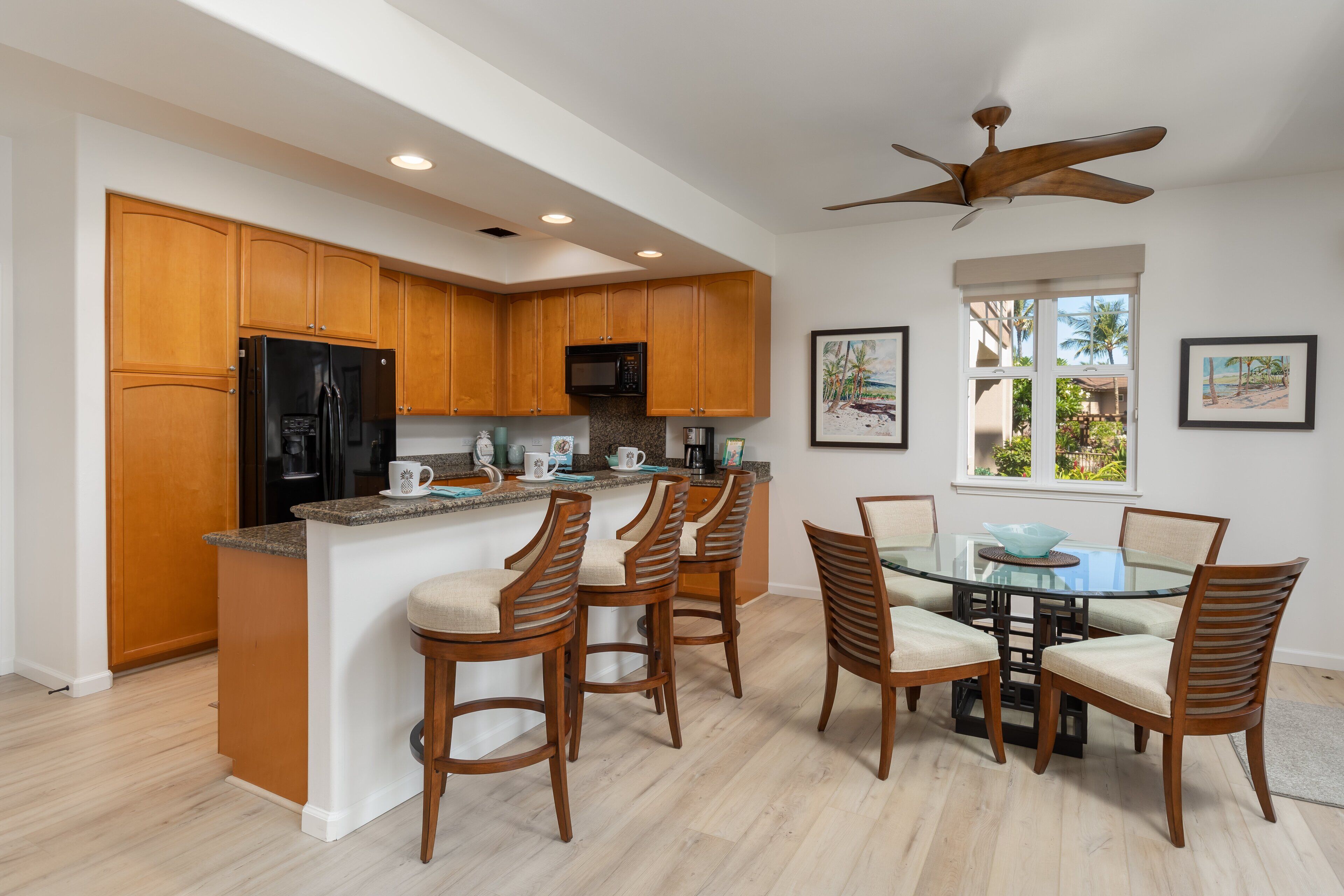 A modern kitchen with wooden cabinets, a black refrigerator, a microwave, and a glass dining table with chairs.