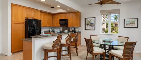 A modern kitchen with wooden cabinets, a black refrigerator, a microwave, and a glass dining table with chairs.