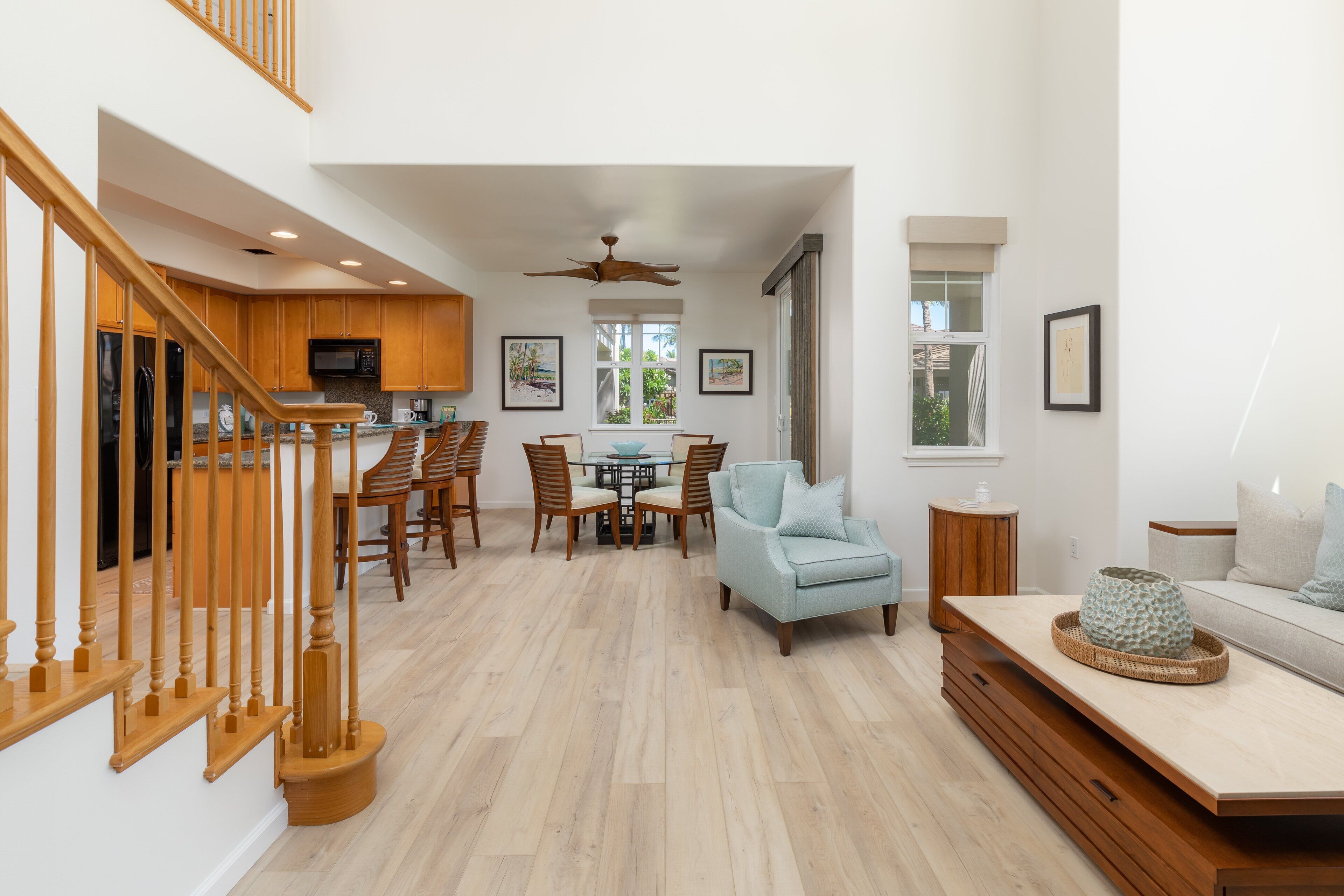 A spacious living area with a wooden staircase, a dining table with chairs, a sofa, and a TV.