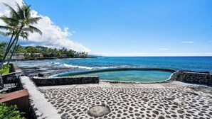 A stone-paved area with a pool, palm trees, and a view of the ocean.