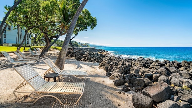 A beach with lounge chairs and a rocky shoreline.