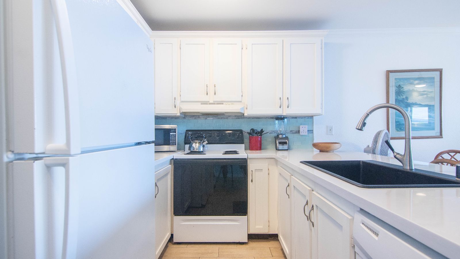 A compact kitchen with white cabinets, a stove, microwave, and a sink.