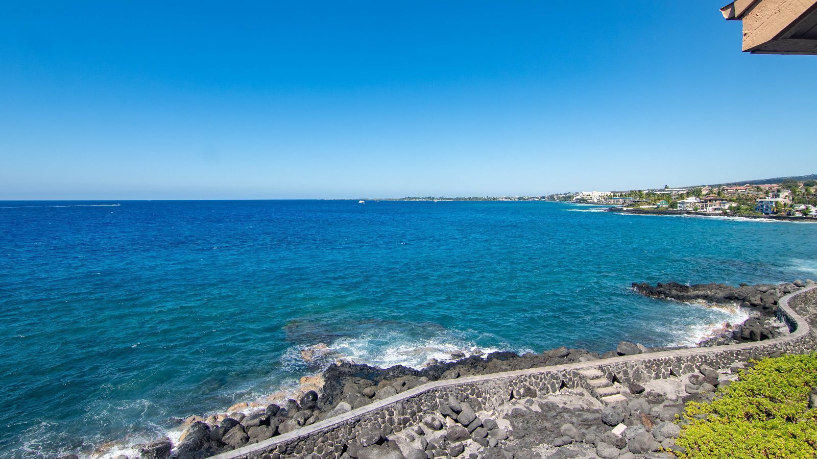 A coastal view with a clear blue sea, rocky shoreline, and a distant town.