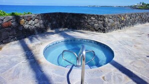 Ein steinerner Pool mit einer Metallleiter, umgeben von einer Steinmauer und freiem Blick auf den Ozean.