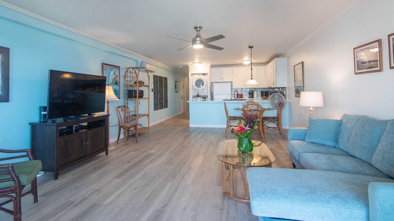 A spacious living room with a flat-screen TV, a sofa, and a coffee table with a vase of flowers.