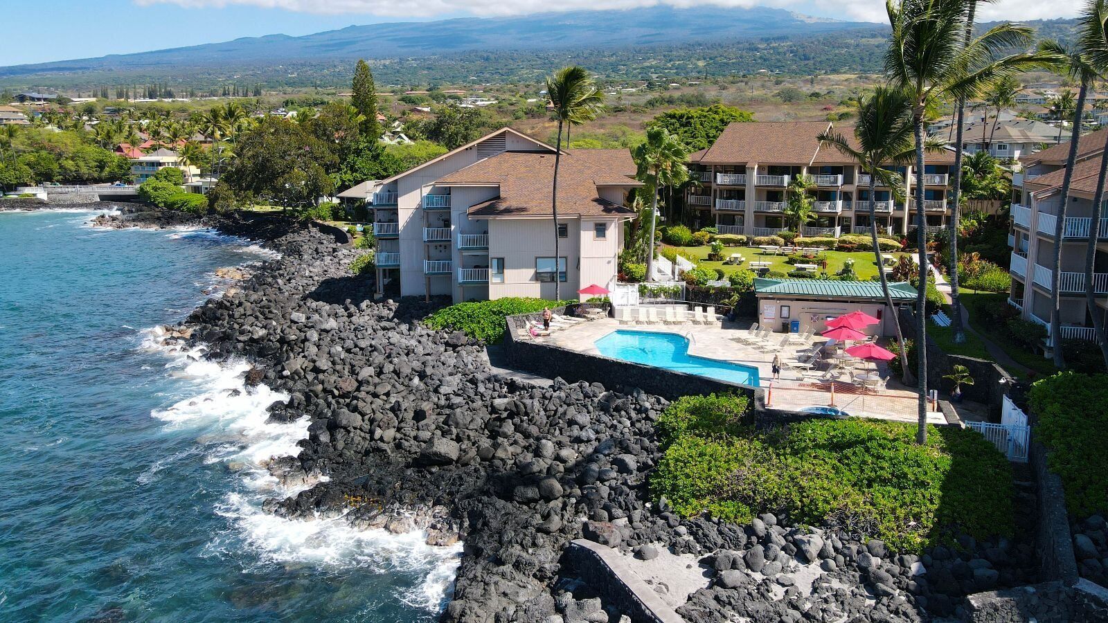A coastal hotel with a pool, multiple balconies, and a view of the ocean.