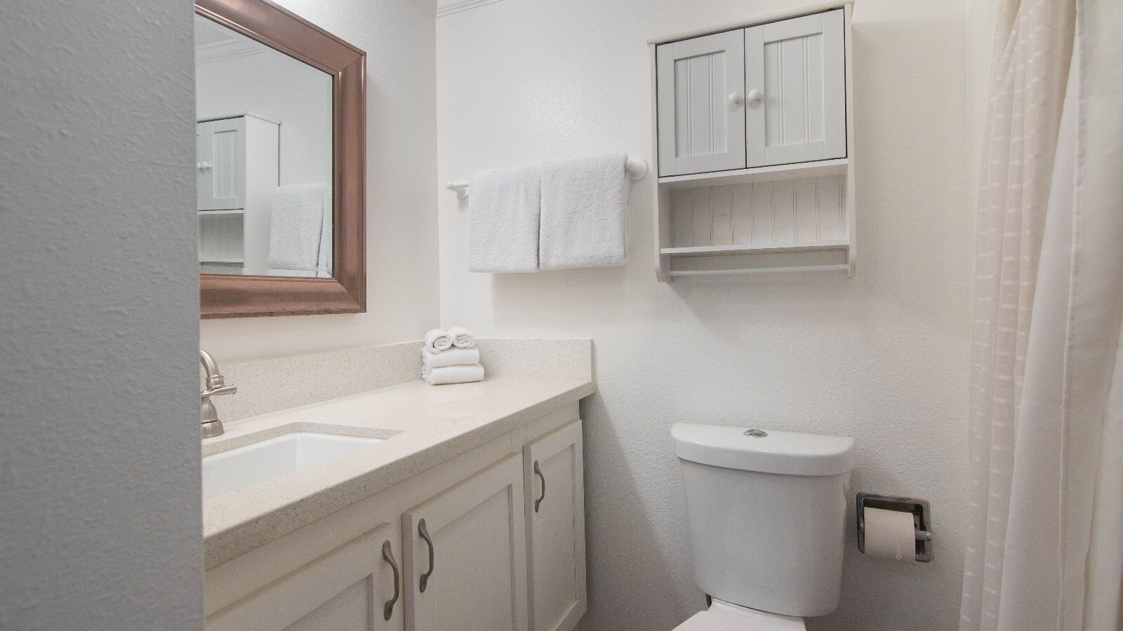 Een badkamer met een wastafel, spiegel, toilet en handdoekhouder.