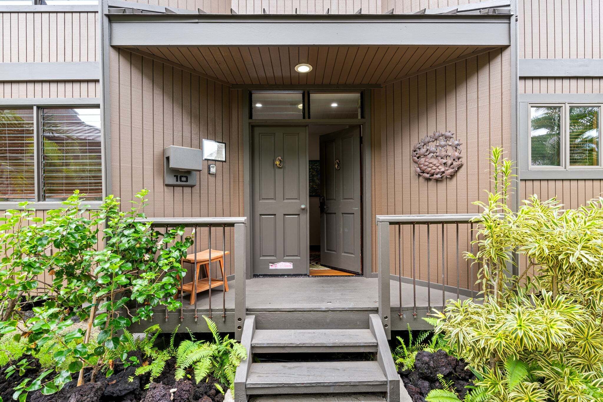 A building entrance with a grey door, a mailbox, and a small outdoor seating area.