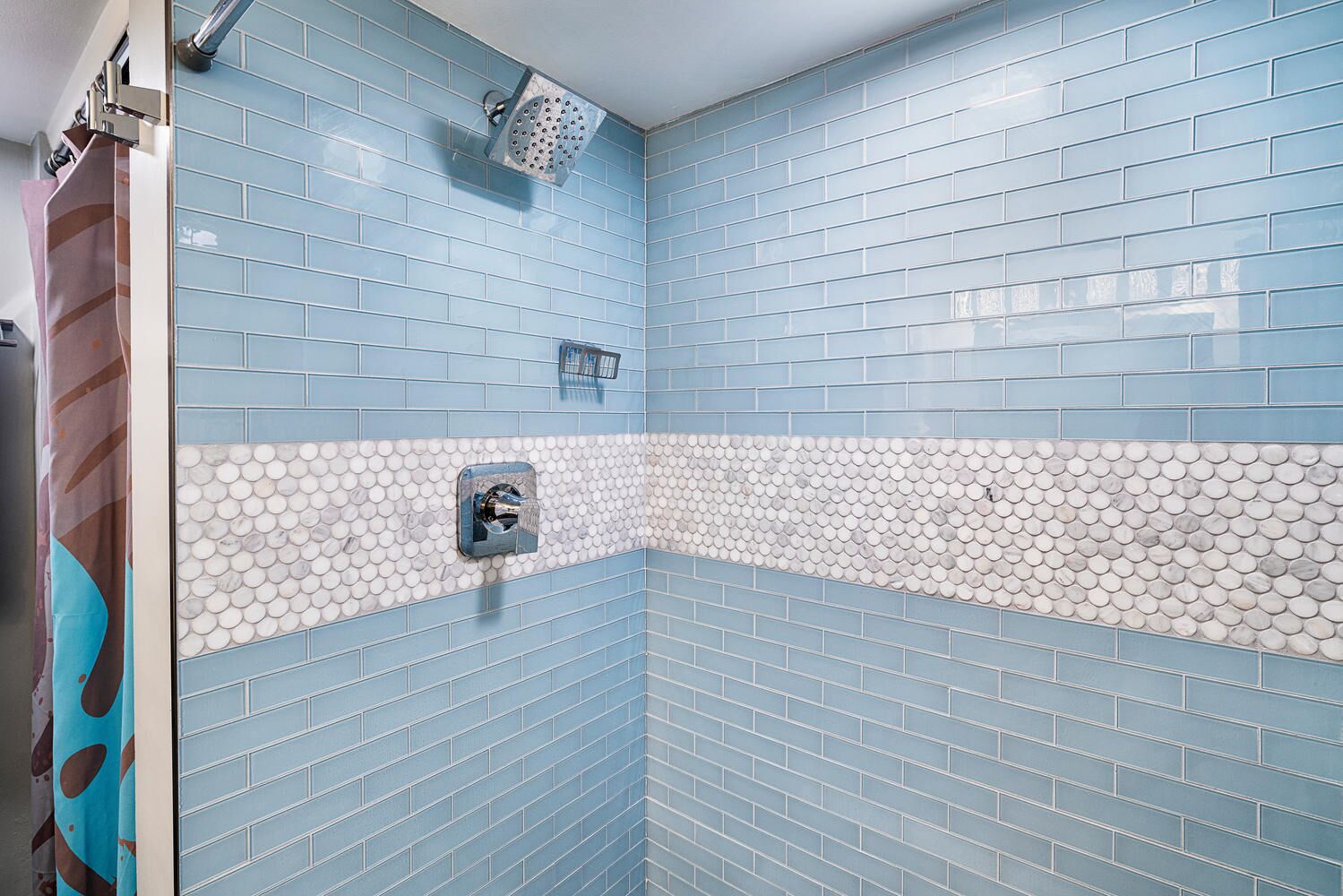 A bathroom with blue-tiled walls, a white and blue mosaic border, and a shower area.