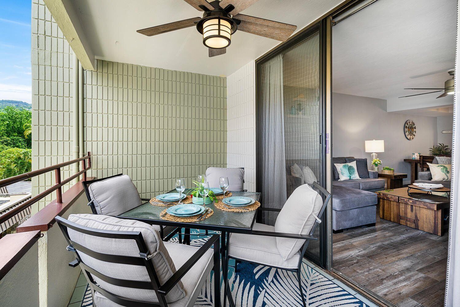 A balcony with a table set for dining, a sofa, and a ceiling fan.