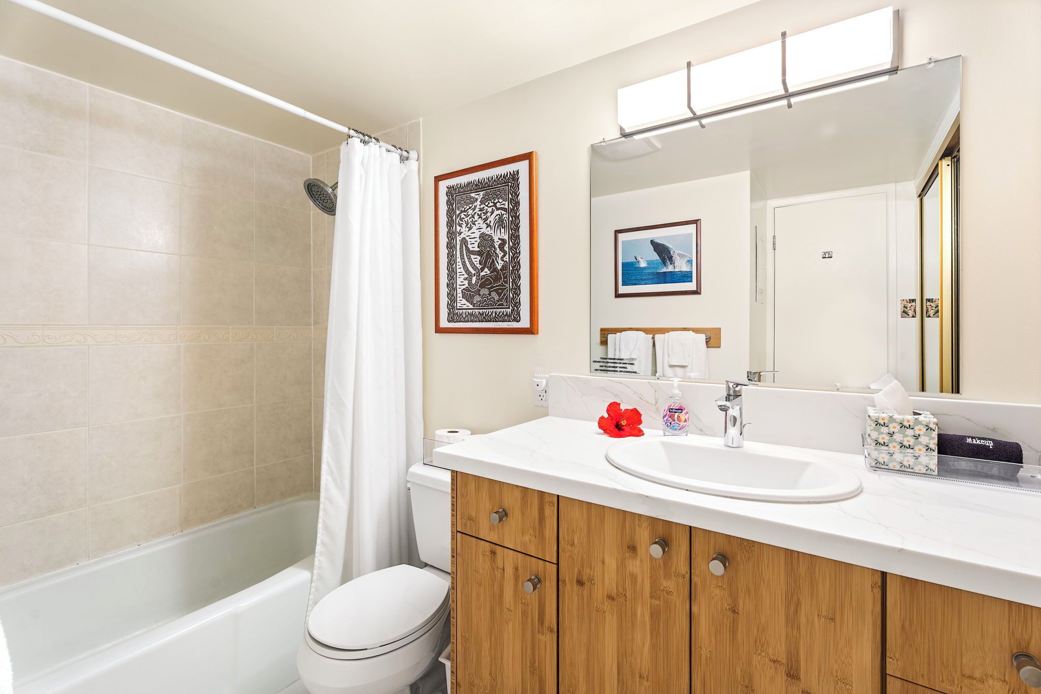 A bathroom with a bathtub, toilet, vanity with a sink, and a large mirror.