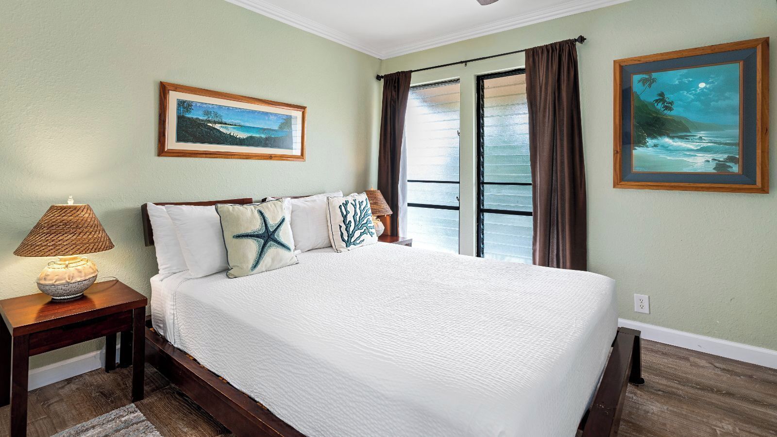A neatly made bed with starfish pillows, a nightstand with a lamp, and two framed pictures on the walls.