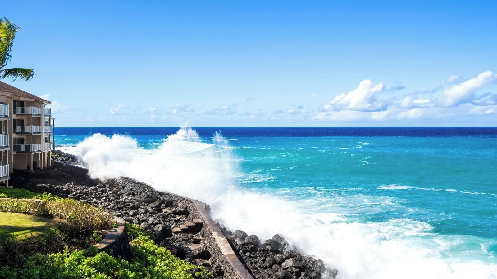 Un hôtel situé sur la côte, avec un rivage rocheux, les vagues de l’océan qui s’écrasent sur le rivage et un ciel bleu dégagé.