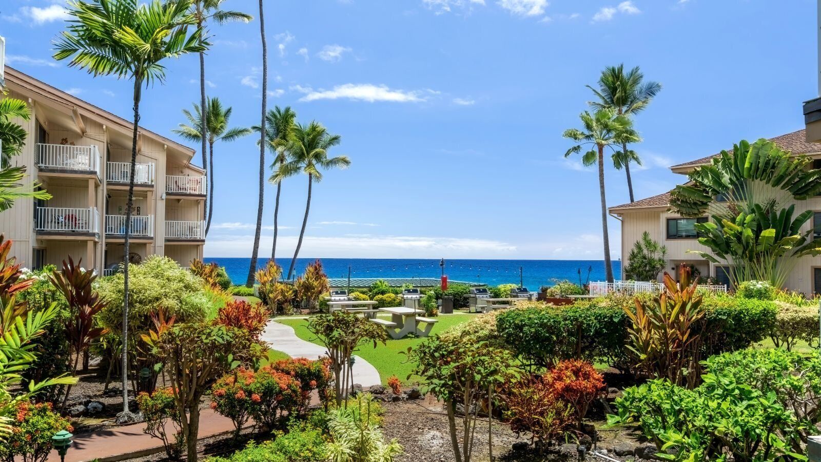A resort with multiple-story buildings, outdoor seating areas, and a view of the ocean.