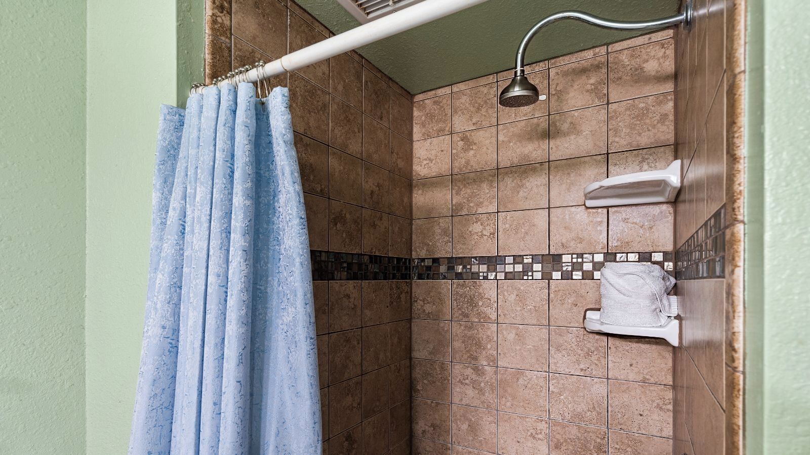 Een douchegedeelte met een blauw douchegordijn, een handdouche en een betegelde wand met een mozaïekrand.