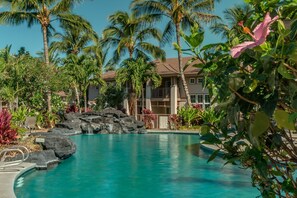 Una piscina de resort con agua azul cristalina, rodeada de palmeras y un edificio con techo de tejas.