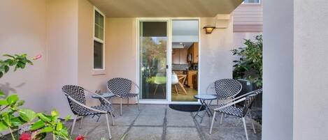 A patio with two chairs and a table, a sliding glass door leading to a kitchen, and potted plants.