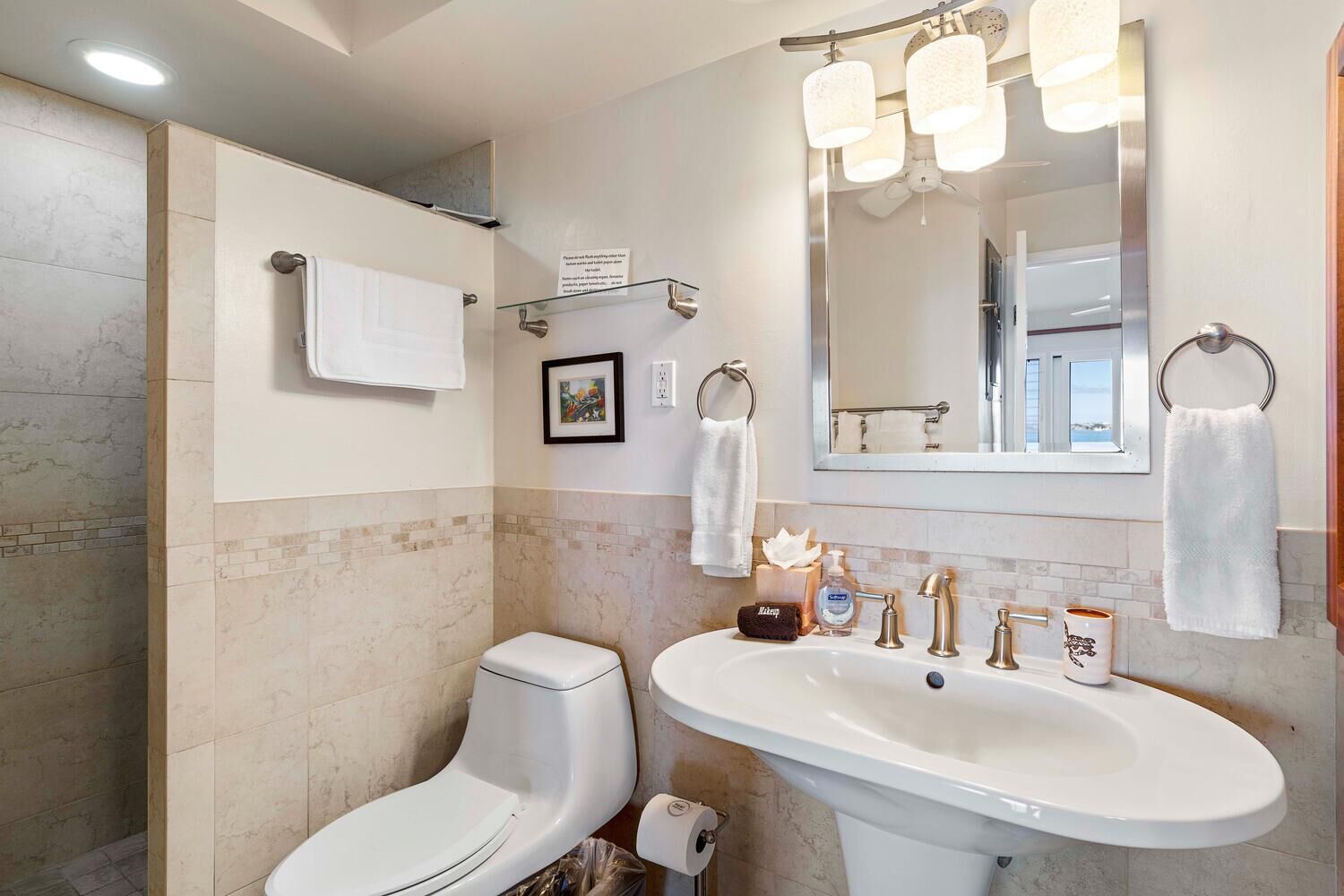 A modern bathroom with a shower, toilet, and sink. There are towels hanging on the wall and a framed picture above the sink.