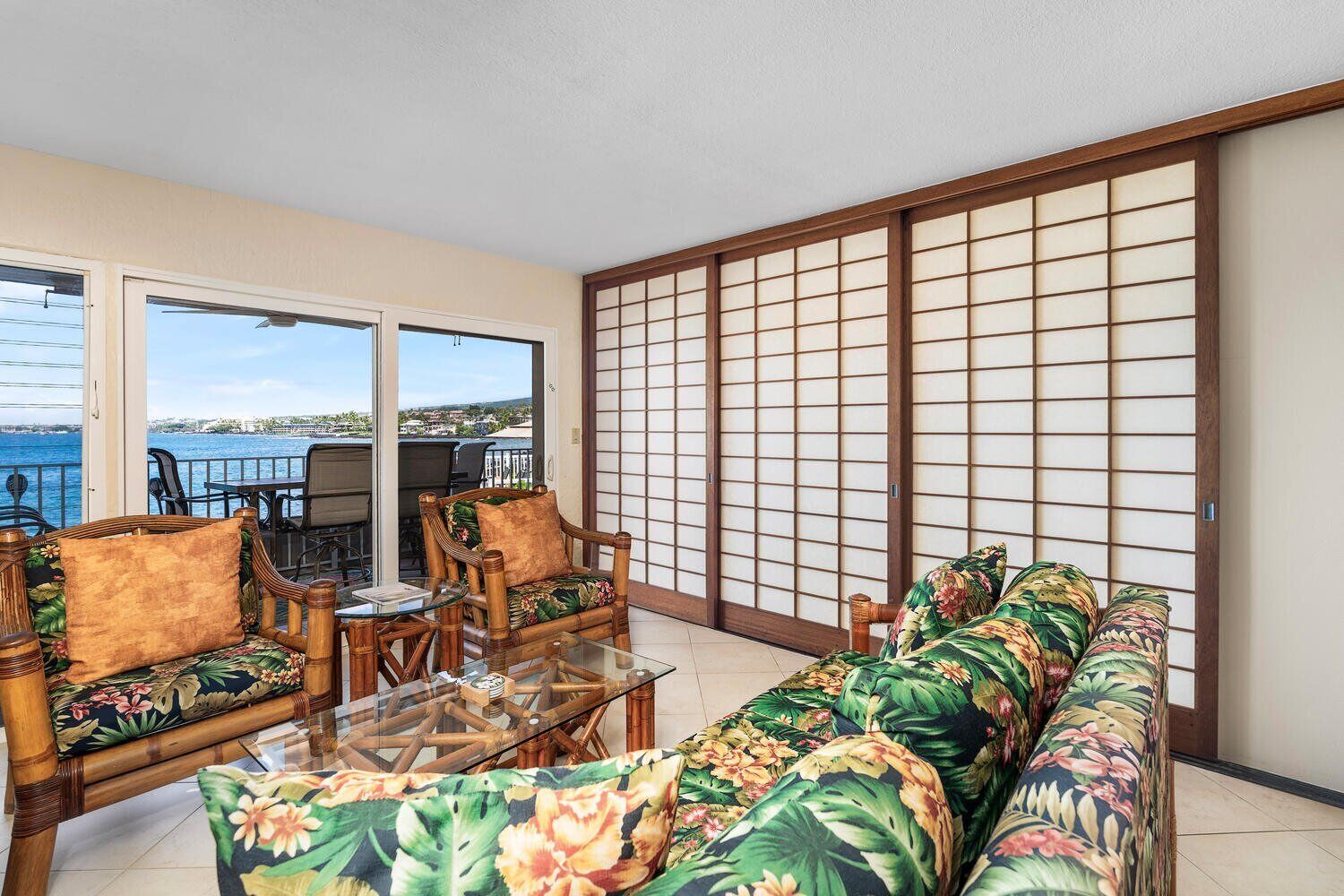 A room with a sofa, chairs, a glass table, and a view of the sea.