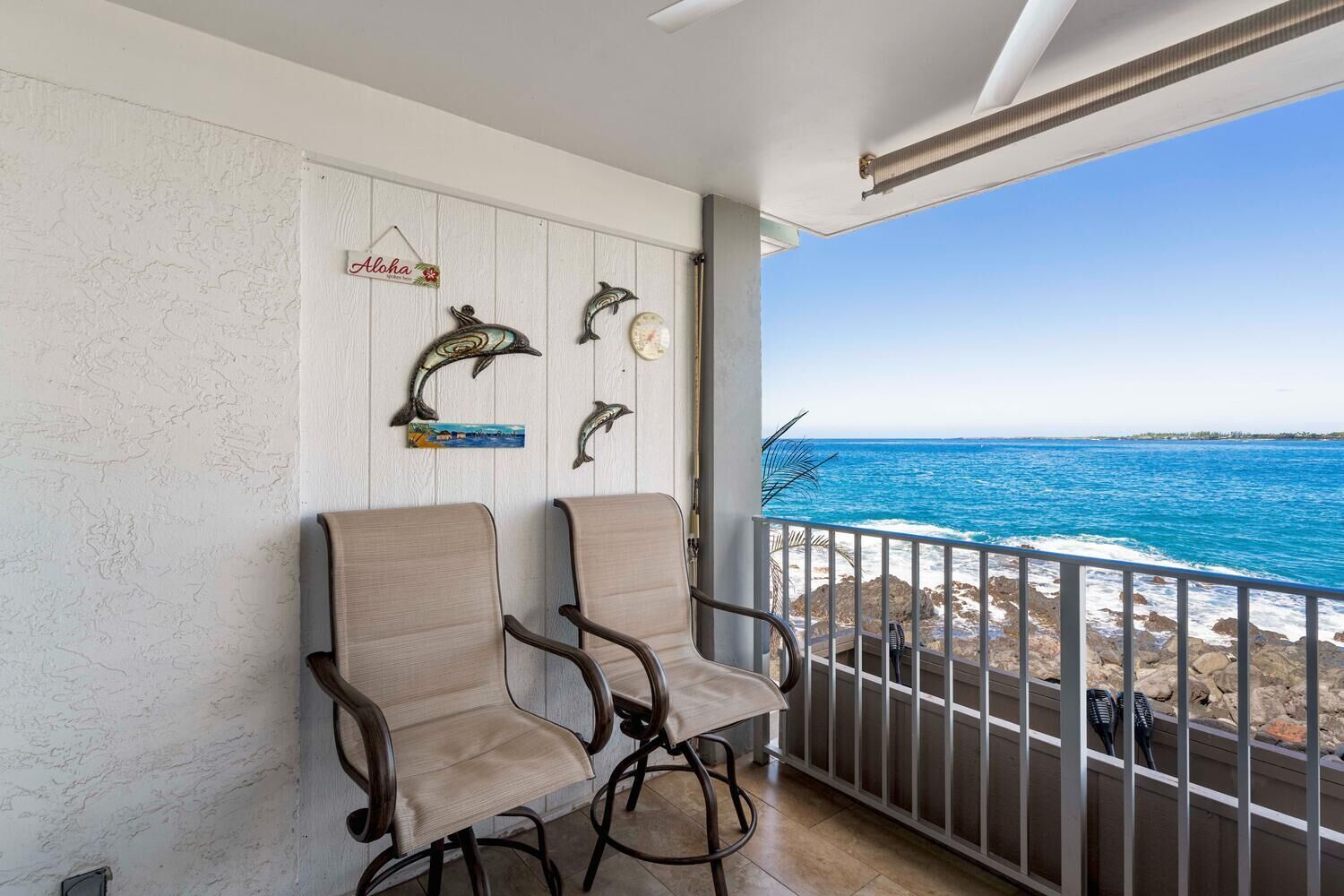 A balcony with two chairs, a decorative wall with dolphin artwork, and a view of the ocean.