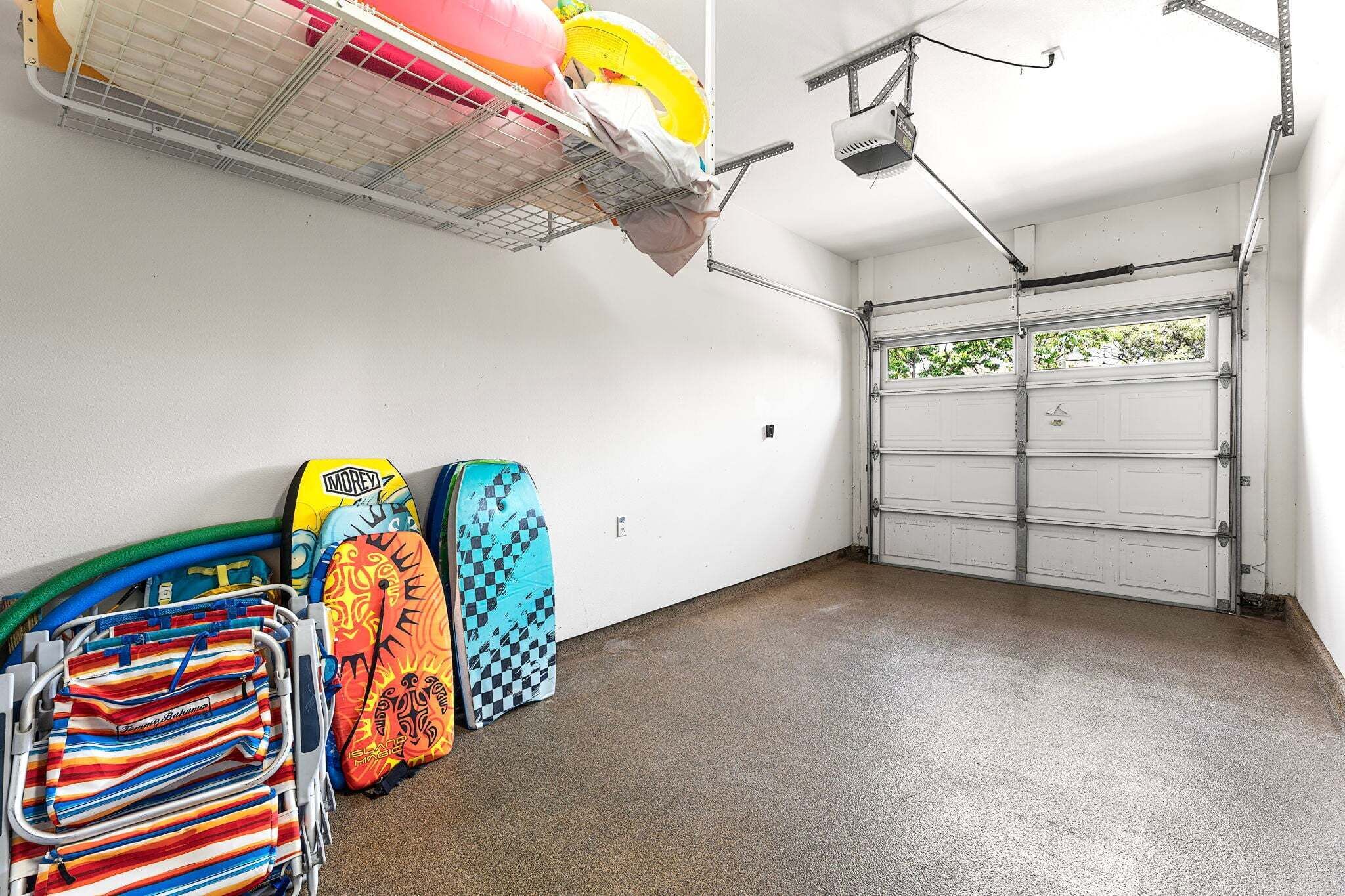 Un garage avec un sol en béton, une porte de garage blanche, et des planches de surf et des serviettes accrochées au mur.