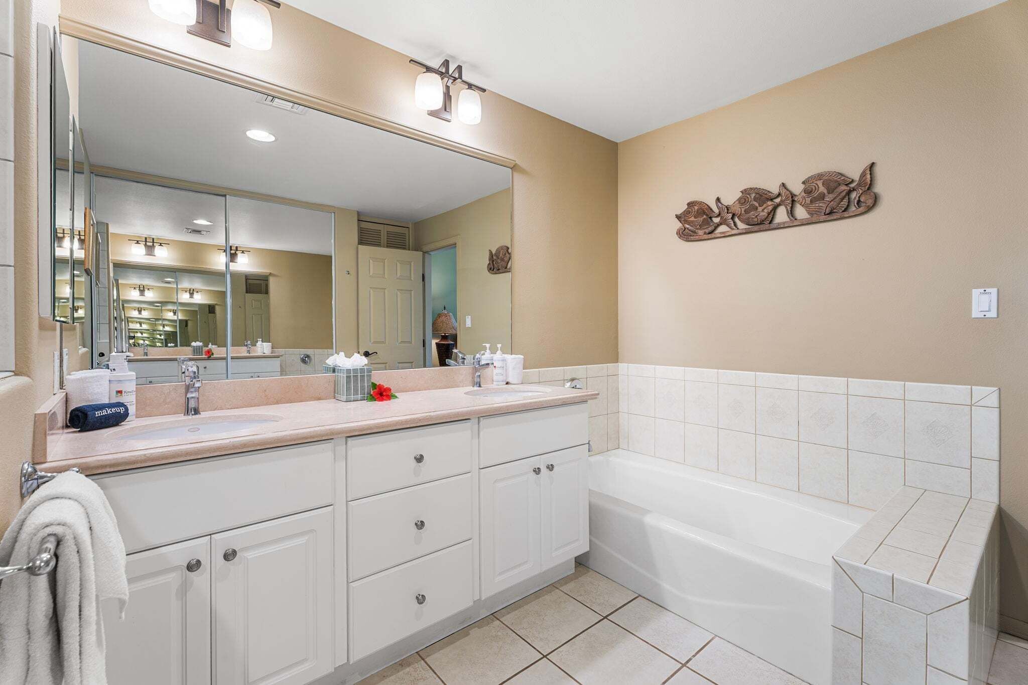 A bathroom with a large mirror, a bathtub, and a vanity with a sink.