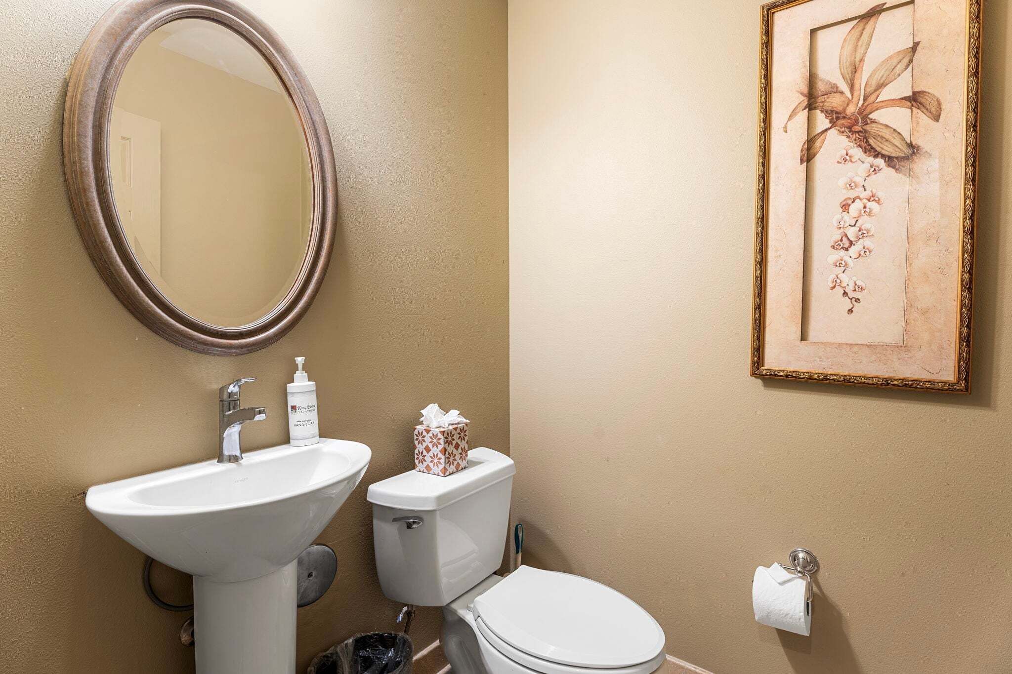 A bathroom with a sink, toilet, and a framed floral artwork on the wall.