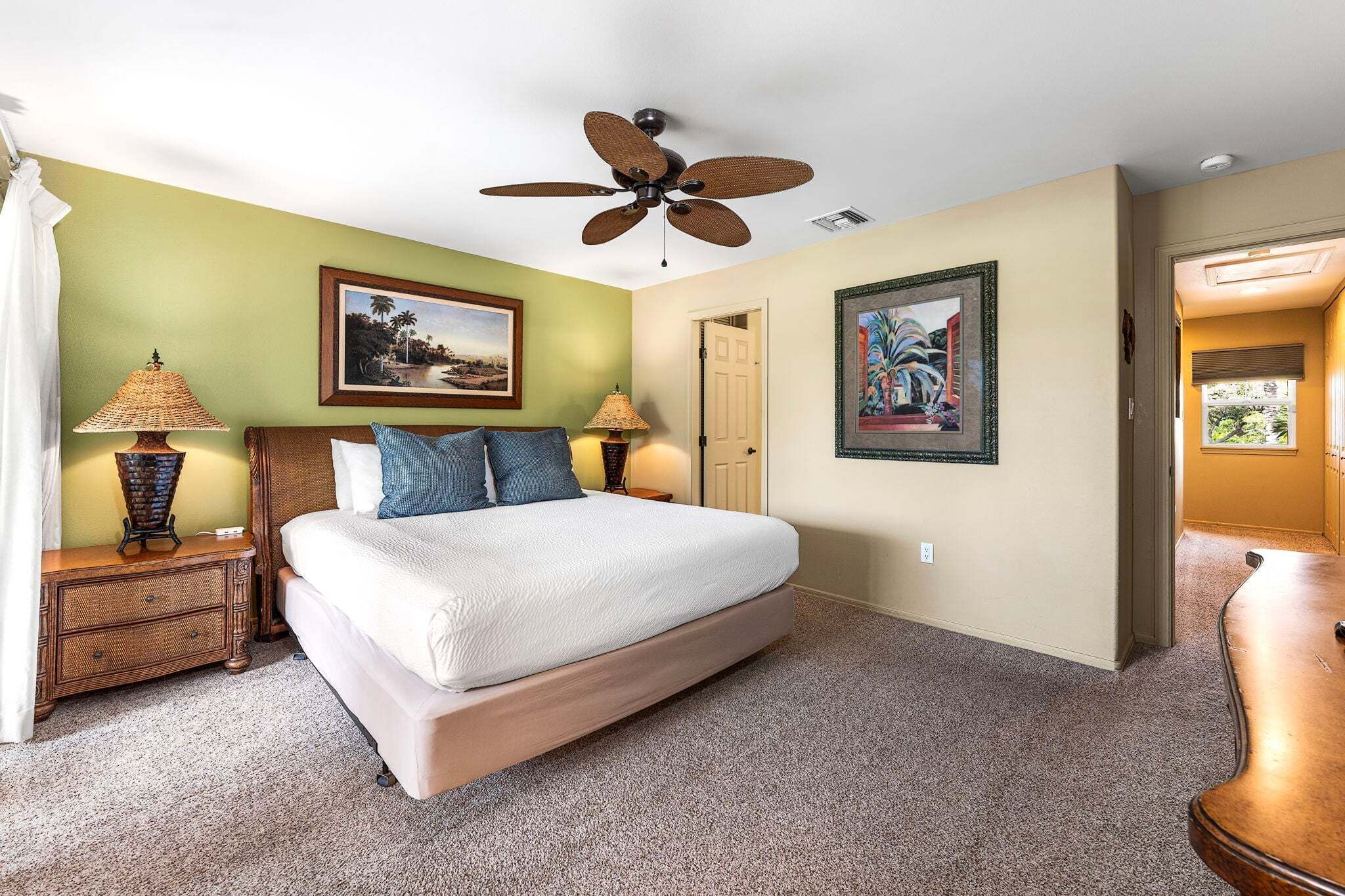 A bedroom with a bed, two bedside lamps, a ceiling fan, and two framed pictures on the walls.