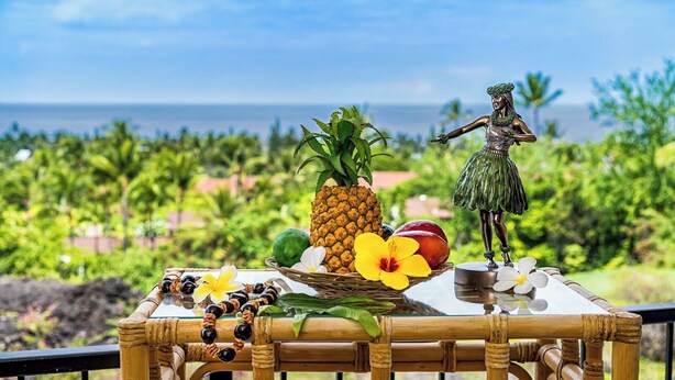 A table with a statue, fruits, and flowers on a balcony overlooking a tropical landscape. - Great Ocean and Golf Course Views - No Stairs - Vrkcv (Kailua-Kona)