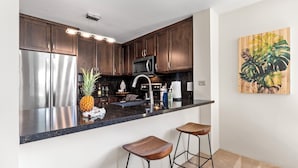 A modern kitchen with dark wooden cabinets, stainless steel appliances, a black countertop, and two wooden bar stools.